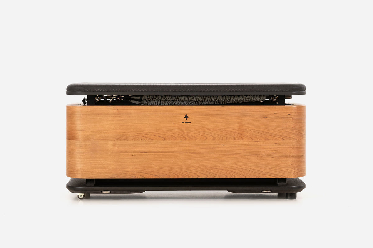 Front view of a warm golden-wood storage bench with the padded lid raised and resistance bands visible inside